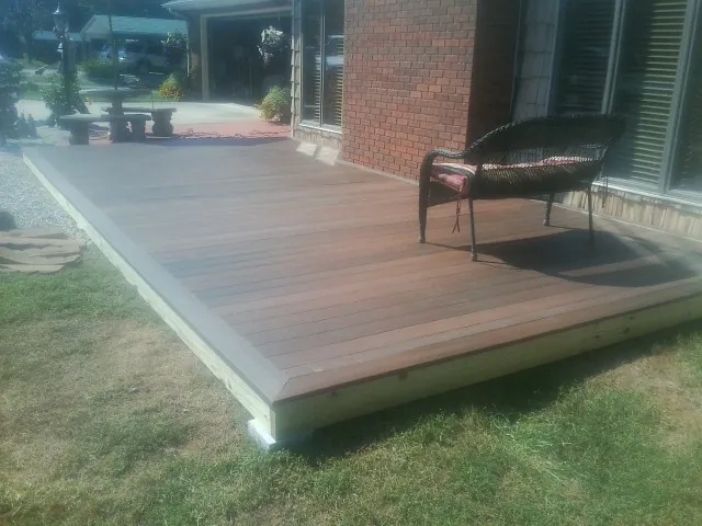 New wood deck and wicker chair beside a brick house in Rogers