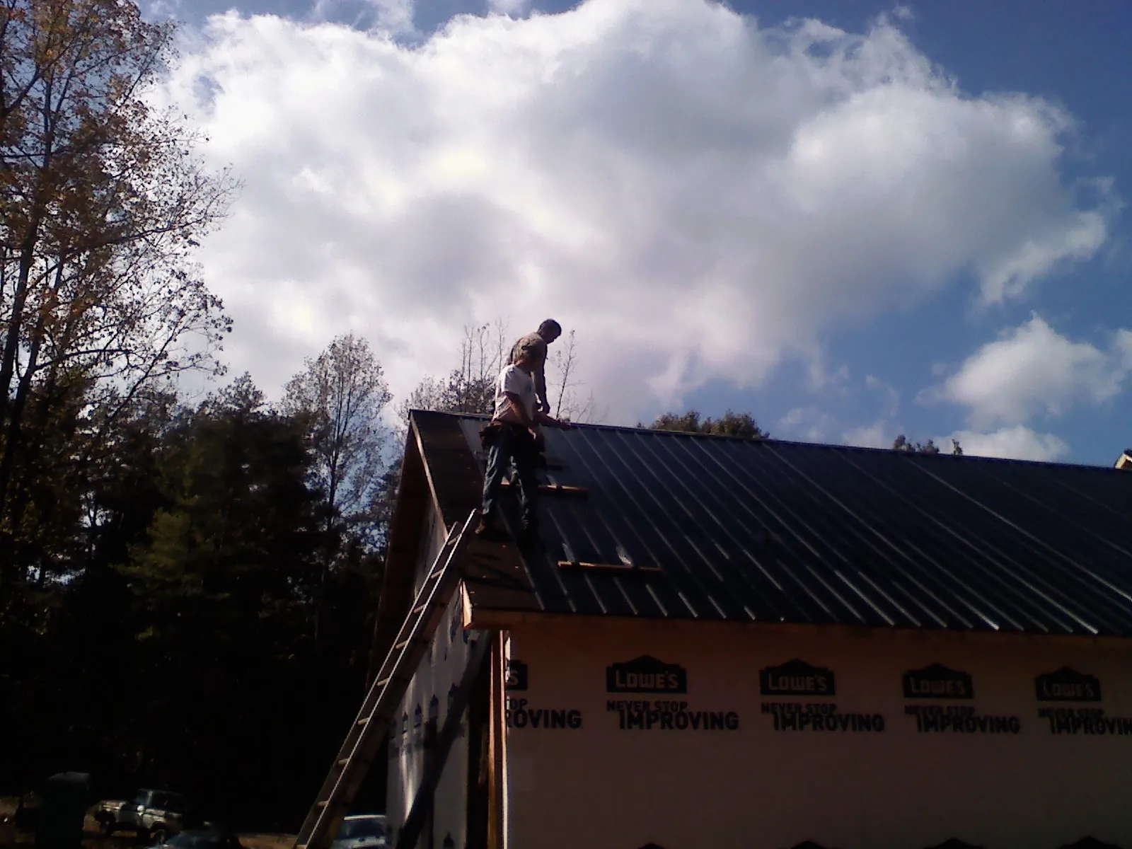 Roofer fastening dark metal panels high against a cloudy sky, from a Roof Inspection job in Rogers