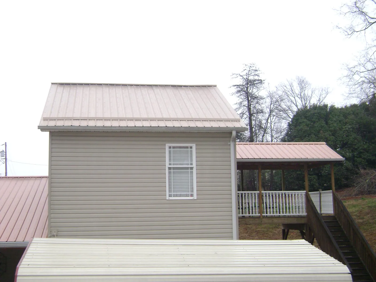 Tan metal roofs on a two story addition and attached porch, from a Roof Replacement job in Rogers