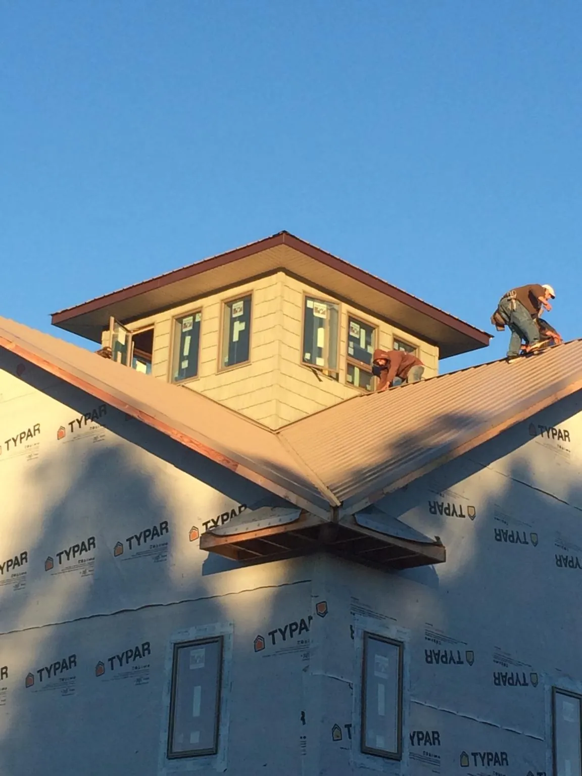 Roofers working around a rooftop cupola on a new metal roof at sunset — Roof Waterproofing in Rogers by Roofing Brothers